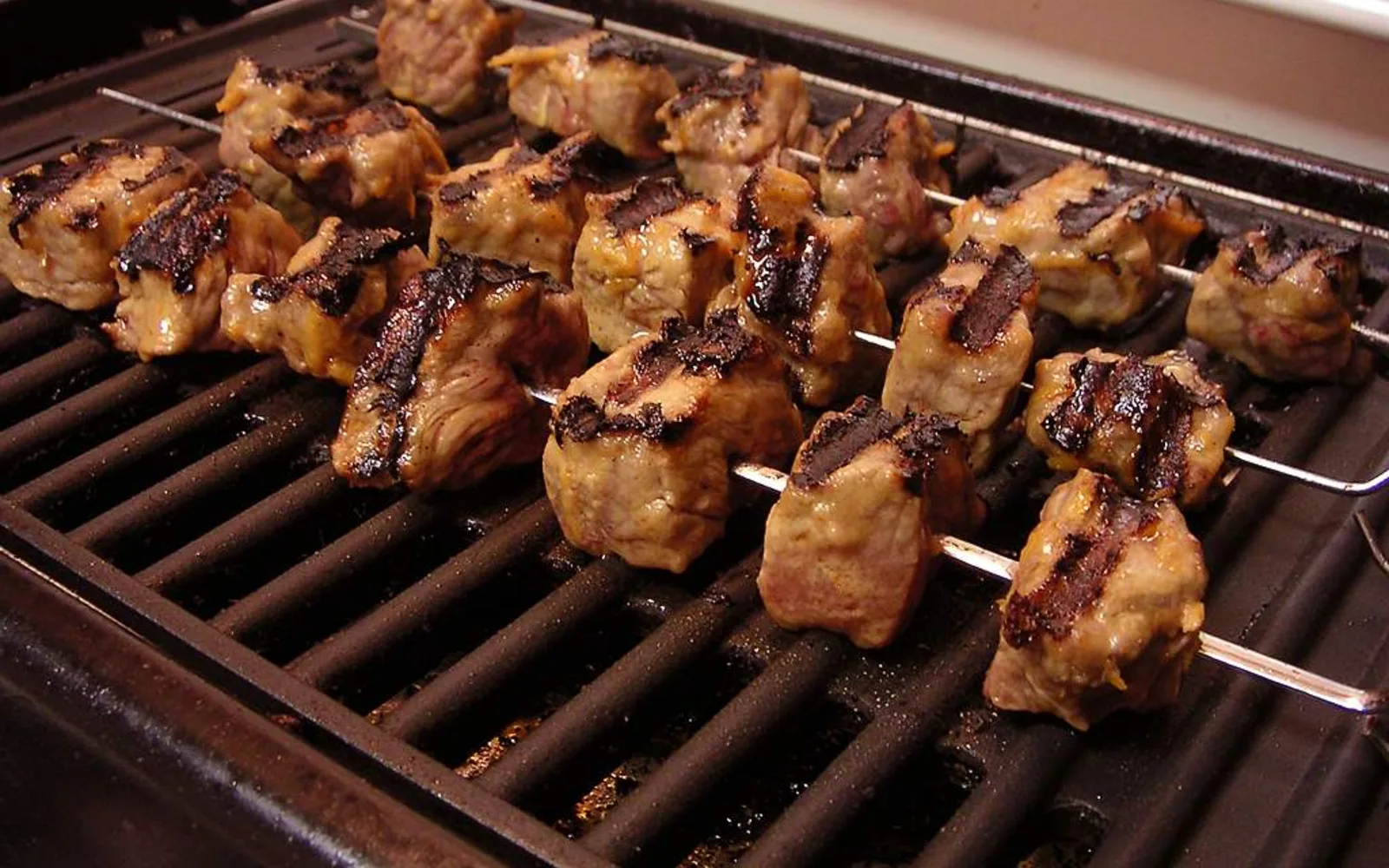 Grilled meat skewers on a barbecue grill with smoke rising